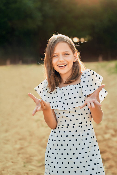 a little girl on the beach in a polka dot dress laughs and puts her hands out to the side - Foto, imagen