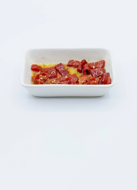 A vertical shot of red spicy pepper slices in a bowl with oil isolated on a white background - Fotoğraf, Görsel