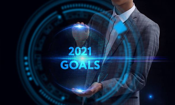 ビジネス、テクノロジー、インターネット、ネットワークの概念。未来の仮想スクリーンで作業し、碑文を見ている若いビジネスマン: 2021目標 - 写真・画像