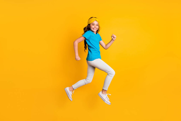 Full length profile photo of funny little lady walking down street jumping high good mood wear casual blue t-shirt headband trousers shoes isolated yellow color background - Fotó, kép
