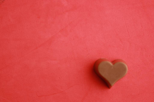 A closeup shot of heart-shaped chocolate on a red background - Fotó, kép