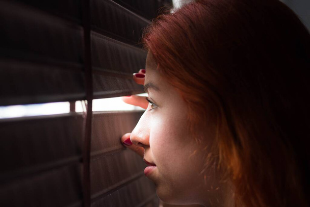 A closeup shot of a young female looking outside behind a closed window - Foto, imagen