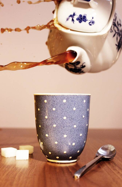 A vertical shot of tea being poured in a mug on the table - Фото, зображення