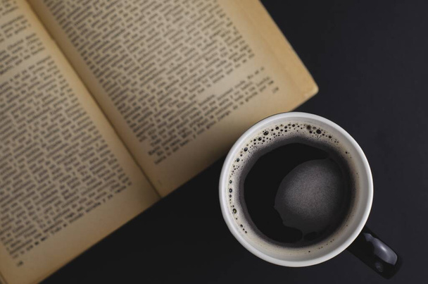Een hoge hoek opname van een kopje koffie en een open boek op de tafel - Foto, afbeelding
