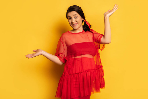 pregnant woman in red tunic looking at camera while standing with open arms on yellow - Foto, immagini