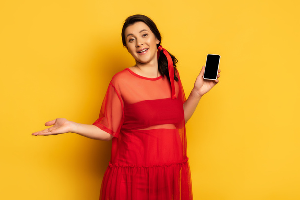 donna incinta in abito rosso in possesso di smartphone con schermo bianco mentre in piedi su giallo - Foto, immagini