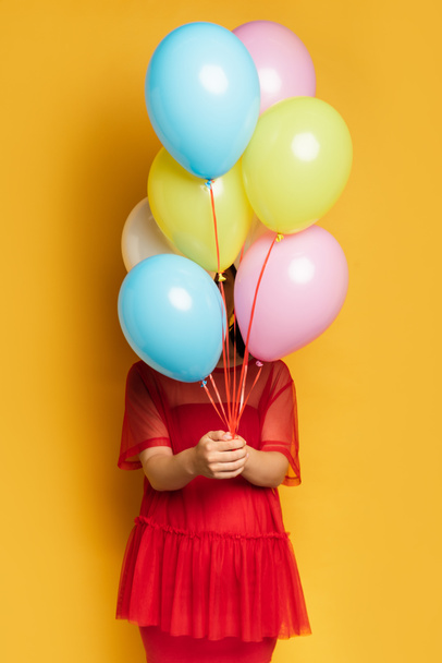 pregnant woman in red outfit obscuring face with colorful festive balloons on yellow - Foto, immagini