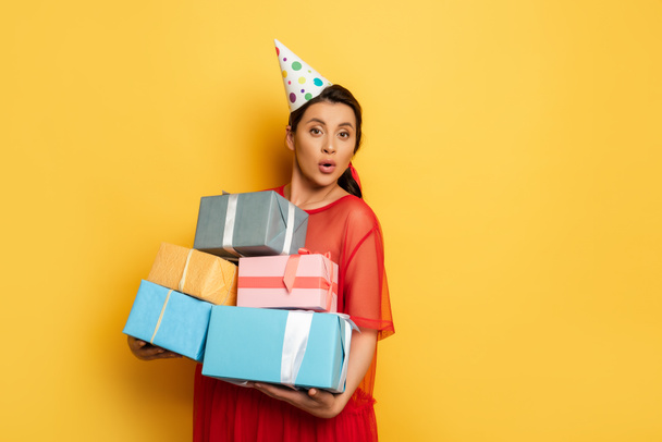 pregnant woman in party car holding stack of gift boxes while looking at camera on yellow - Photo, Image