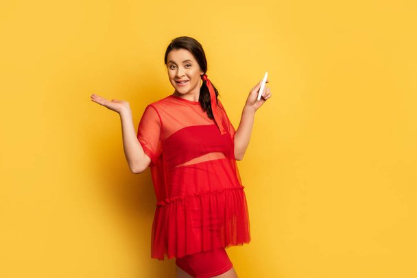pregnant woman in red outfit holding pregnancy test while standing on yellow - Photo, Image