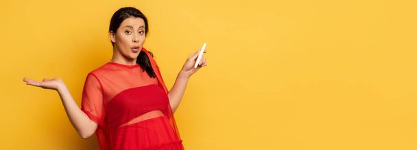 horizontal image of confused pregnant woman showing shrug gesture while holding pregnancy test on yellow - Foto, Imagem