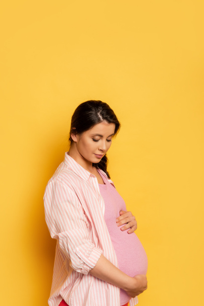 brunette pregnant woman touching belly while standing on yellow - Photo, Image