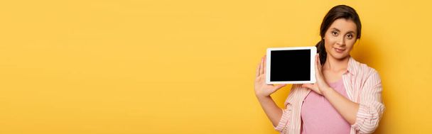 panoramic shot of pregnant woman showing digital tablet with blank screen on yellow - Photo, image