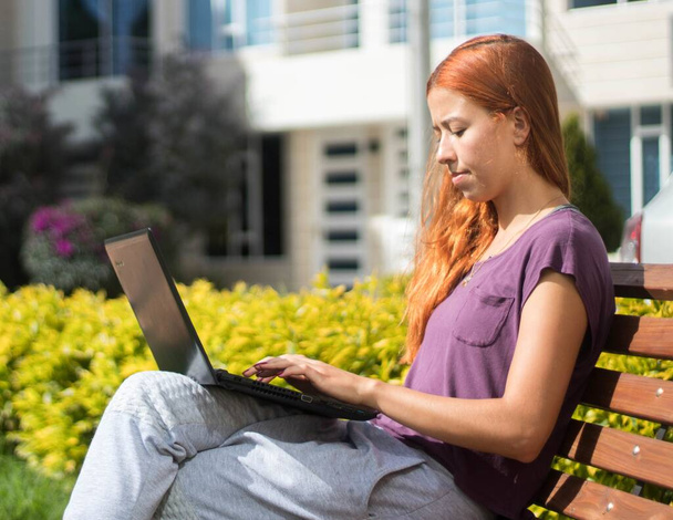 A young female working/studying on her computer outdoors at daytime - Foto, Imagen
