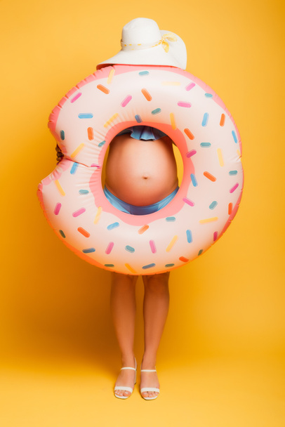 těhotná žena v slamáku skrývající se za plavecký prsten na žluté - Fotografie, Obrázek