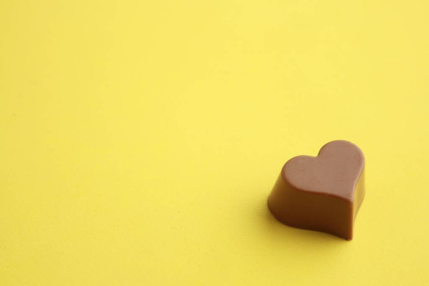 Ένα σοκολατένιο γλυκό με σχήμα καρδιάς σε κίτρινο φόντο - Φωτογραφία, εικόνα