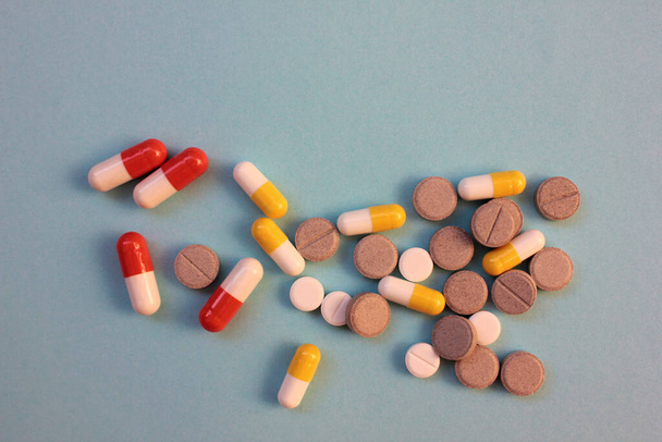 Veelkleurige pillen en capsules op blauwe achtergrond met kopieerruimte. Bovenaanzicht, selectieve focus - Foto, afbeelding