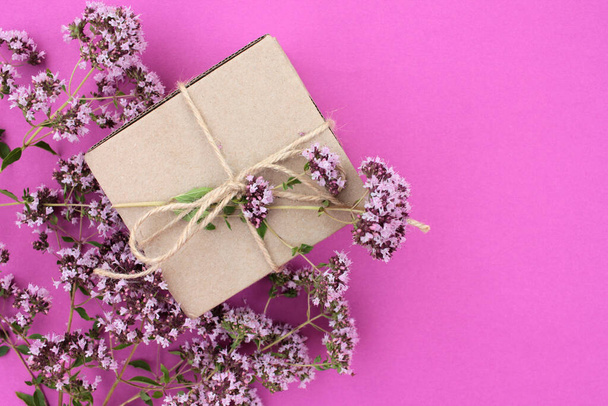 Coffret cadeau marron avec des fleurs de marjolaine douce sur fond violet avec espace de copie. Vue de dessus, mise au point sélective - Photo, image