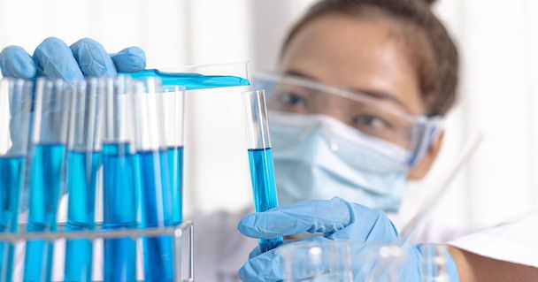Scientists are carrying blue chemical test tubes to prepare for the determination of chemical composition and biological mass in a scientific laboratory, Scientists and research in the lab Concept. - Photo, image