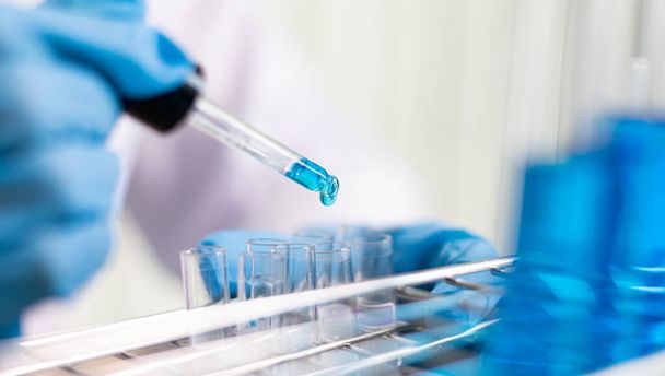 Wissenschaftler tragen blaue chemische Reagenzgläser, um sich in einem wissenschaftlichen Labor auf die Bestimmung der chemischen Zusammensetzung und der biologischen Masse vorzubereiten.. - Foto, Bild