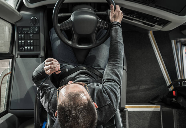 Общественный транспорт. Кавказский тренер-водитель автобуса за рулем автомобиля, разговаривает с пассажирами, используя систему автобусного интеркома. Вид сверху. - Фото, изображение