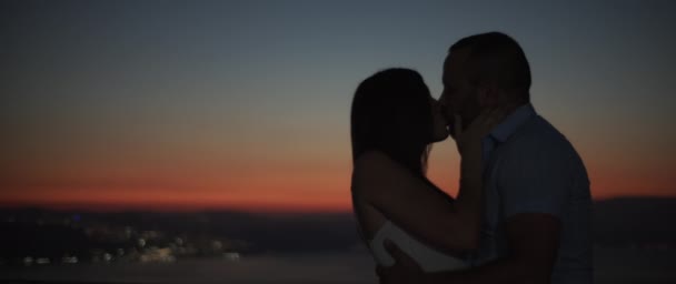 Silhueta de um casal beijando ao pôr do sol com luzes da cidade noite no fundo. Movimento lento, DOF raso
. - Filmagem, Vídeo