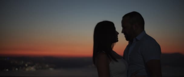 Silhouette of a couple kissing at sunset with night city lights at the background. Slow motion, Shallow DOF. - Footage, Video