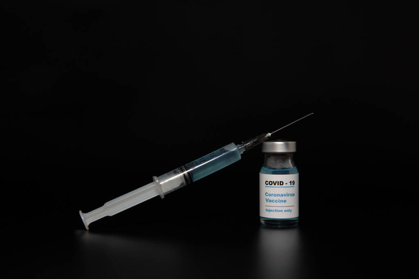 Frasco de vacina pequena (phial) com um rótulo que dizia "Covid - 19 Corona vírus Injeção de vacina apenas" & uma seringa médica isolada em preto Vacinação para prevenção, imunização e tratamento do vírus
 - Foto, Imagem