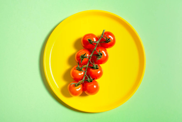 Pomidor wiśniowy na żółtym talerzu na zielonym. Koncepcja. Warzywa. Cień. - Zdjęcie, obraz