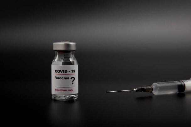Petit flacon de vaccin (phial) avec une étiquette portant la mention "Covide - 19 Vaccin" et un point d'interrogation et une seringue médicale isolée sur fond noir Vaccination pour la prévention, la vaccination et le traitement - Photo, image