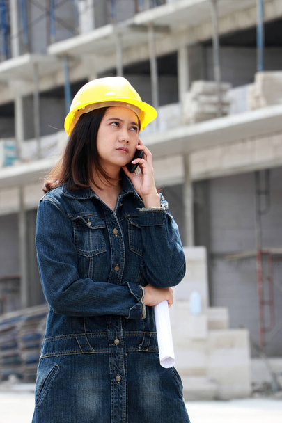 黄色のヘルメットを持つ女性土木技術者や建築家,立って、作業領域で手を取りながら、携帯電話やプロジェクトの草案を呼び出します. - 写真・画像