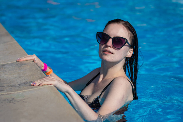 A young girl in sunglasses swims in the pool. Beautiful woman resting in the water in the outdoor pool - Photo, image