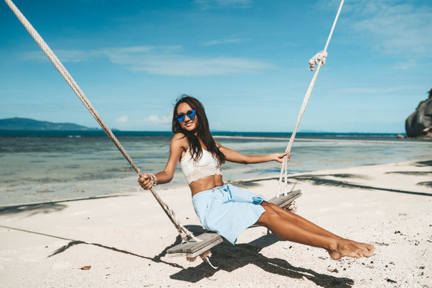 Woman in blue skirt and white top swinging at tropical beach in Thailand - Фото, изображение