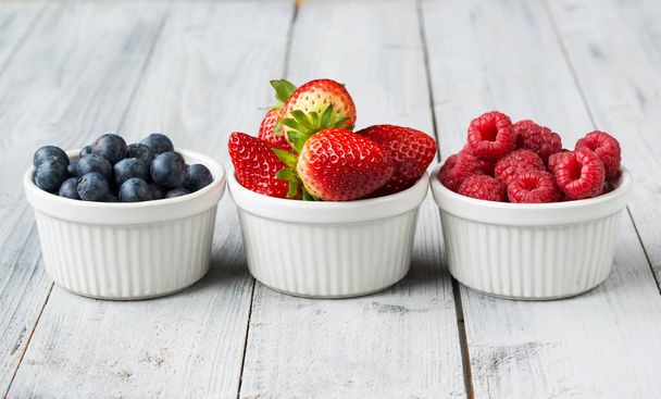 Assorted fresh juicy berries in three tiny bowls, blueberry, strawberry and raspberry - Zdjęcie, obraz