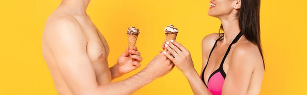 panoramic crop of happy girl taking ice cream near muscular man isolated on yellow - Foto, imagen