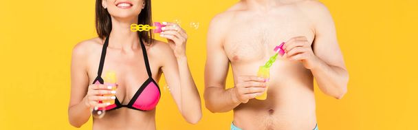 panoramic crop of happy girl in swimsuit near shirtless man and soap bubbles isolated on yellow  - Foto, Bild