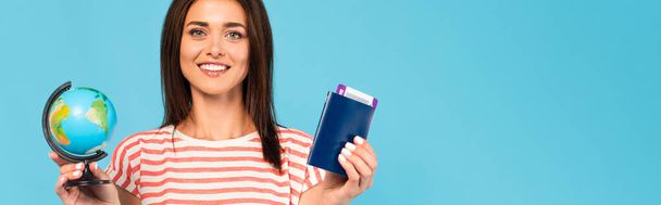 οριζόντια εικόνα του χαρούμενου κοριτσιού που κατέχει διαβατήριο και σφαίρα απομονωμένη στο μπλε - Φωτογραφία, εικόνα