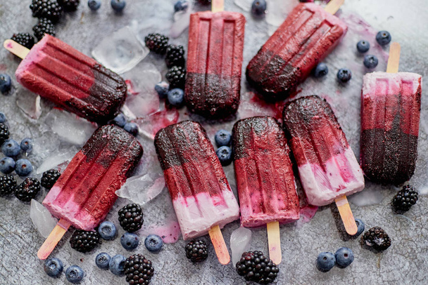 Homemade blackberry and cream ice-creams or popsicles with frozen berries on black slate tray - 写真・画像