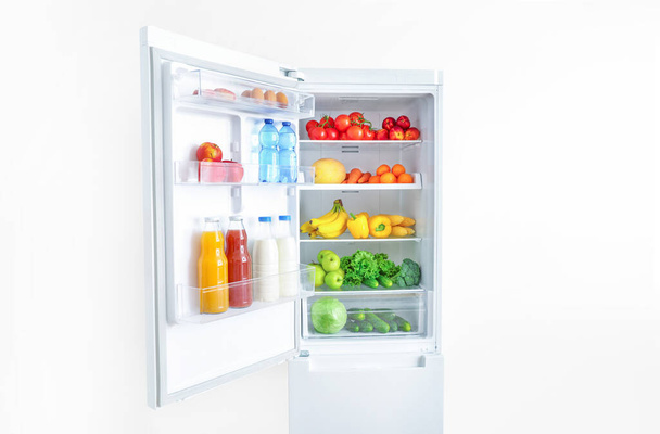 Open fridge full of vegetables, fruits and drinks on white wall background. - Fotoğraf, Görsel