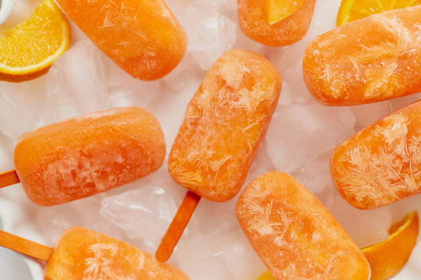 Paletas congeladas caseras hechas con naranjas frescas orágicas colocadas con cubitos de hielo en la mesa de mármol - Foto, Imagen