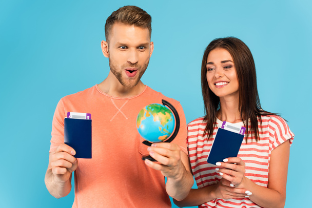 ευτυχισμένο ζευγάρι κοιτάζοντας την υδρόγειο, ενώ κατέχουν διαβατήρια απομονώνονται σε μπλε - Φωτογραφία, εικόνα