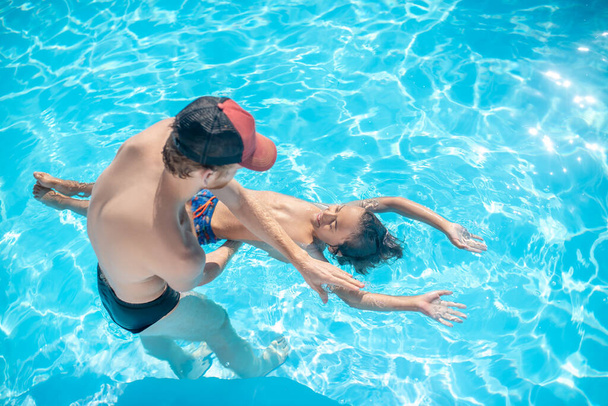 Valmentaja opettaa poikaa pysymään vedessä uima-altaassa. - Valokuva, kuva