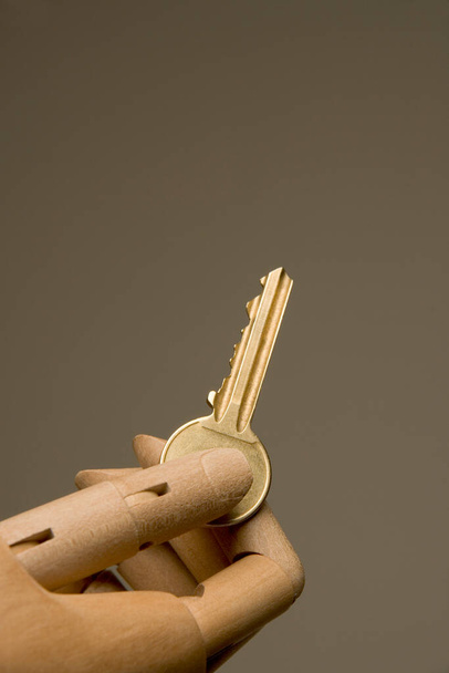 Een kunstenaar mannequin hand presenteren een huis deur sleutel op een effen achtergrond - Foto, afbeelding
