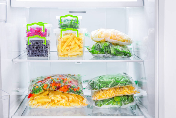 Packages and containers with frozen fruits and vegetables in freezer. - Photo, Image