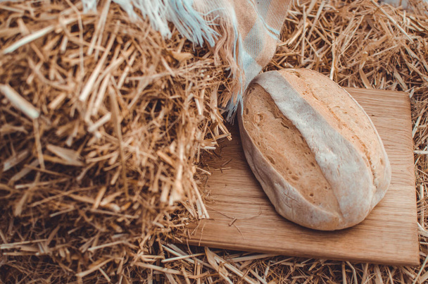 Pšeničný chléb na dřevěné desce proti slámě ze zlaté pšenice. Přírodní pozadí.Detail chleba na papíře a dřevěné deskě.Čerstvě upečený aromatický pšeničný chléb  - Fotografie, Obrázek
