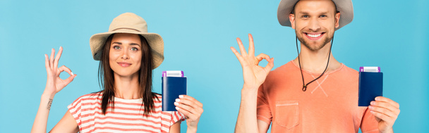 panoramic shot of happy man and woman in hats holding passports and showing ok sign isolated on blue - Photo, Image
