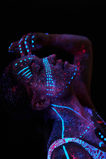 Umělecká dívka kosmos v ultrafialovém světle. Žena dělá jógu, zahřívá se. Celé tělo je pokryto barevnými kapkami. Astrální jóga. Hluk, rozostřený - Fotografie, Obrázek