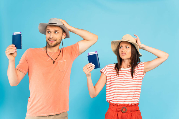 homme et femme confus touchant des chapeaux et tenant des passeports sur bleu - Photo, image