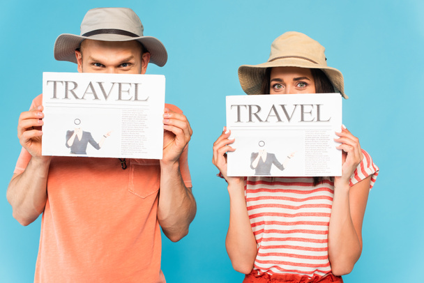 Şapkalı çift, mavi üzerine izole edilmiş seyahat gazeteleriyle yüzlerini kapatıyor.  - Fotoğraf, Görsel