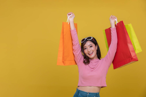 Asyalı güzel, mutlu, neşeli bir genç kadın portresi sarı arka planda izole edilmiş alışveriş çantaları taşıyor. Mutluluk, tüketim, satış ve alışveriş danışmanları. - Fotoğraf, Görsel