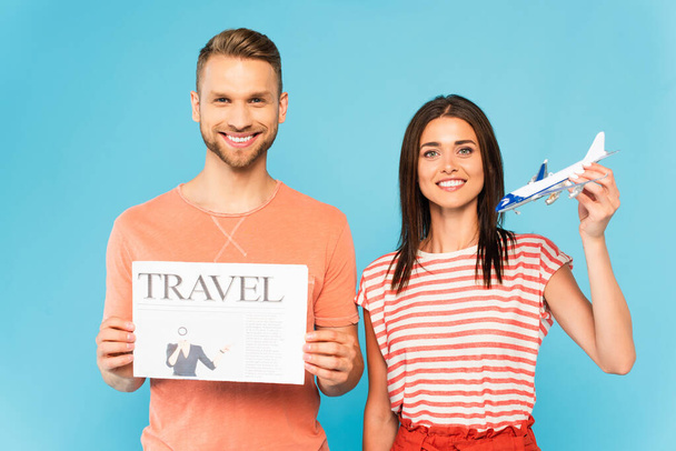femme heureuse tenant jouet avion près homme barbu avec journal de voyage isolé sur bleu - Photo, image